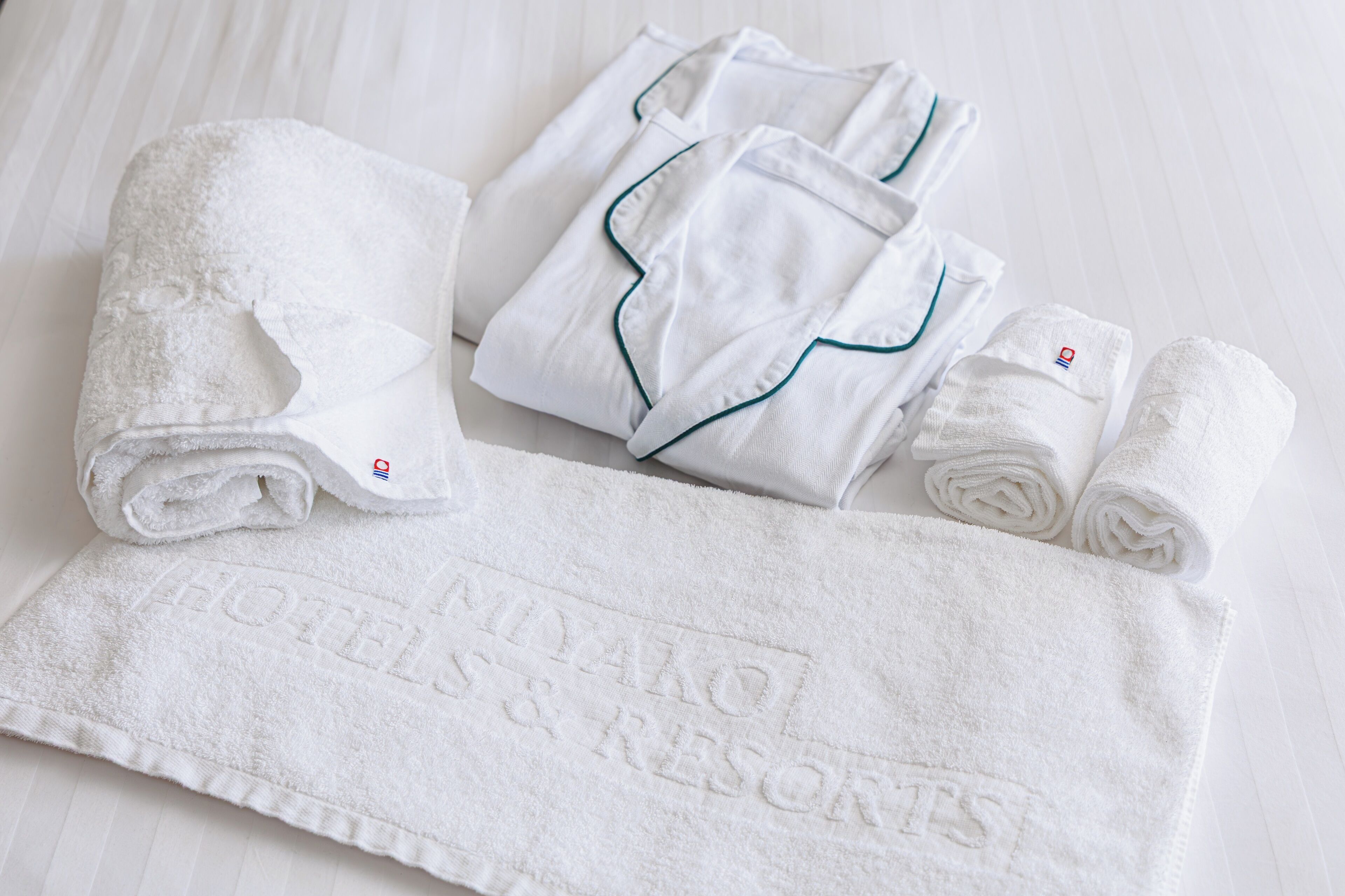 Un set ordinato di asciugamani e accappatoi bianchi con ricami, tipico di un hotel o resort.
