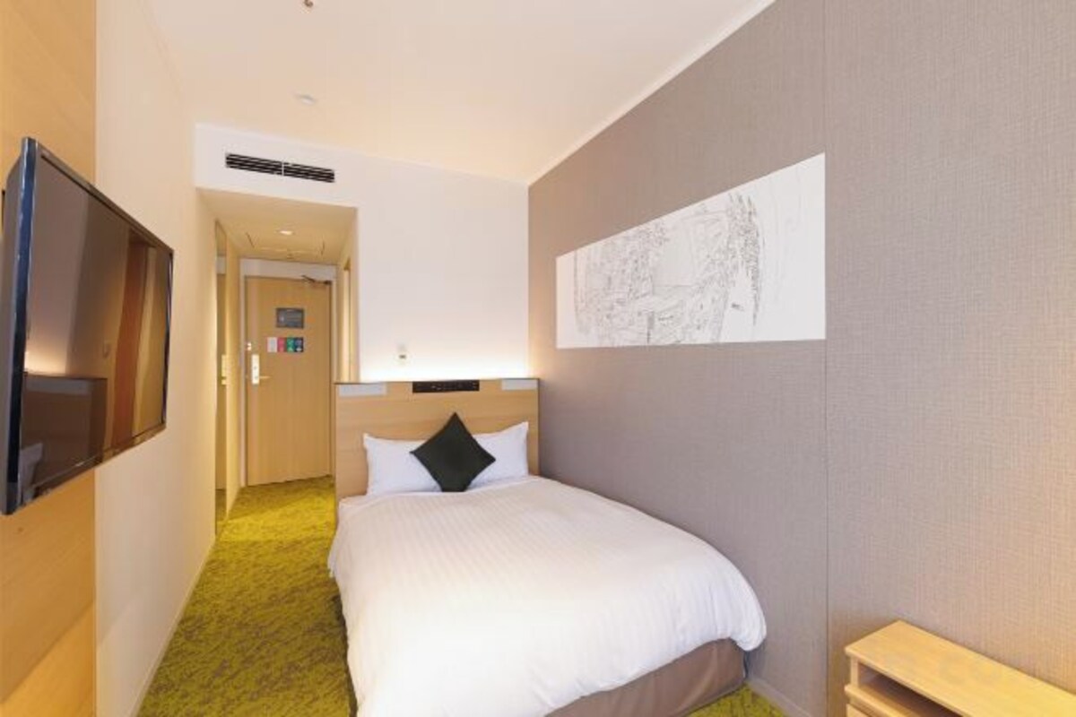 A hotel room with a bed, a television, a map on the wall, and a door leading to another room.