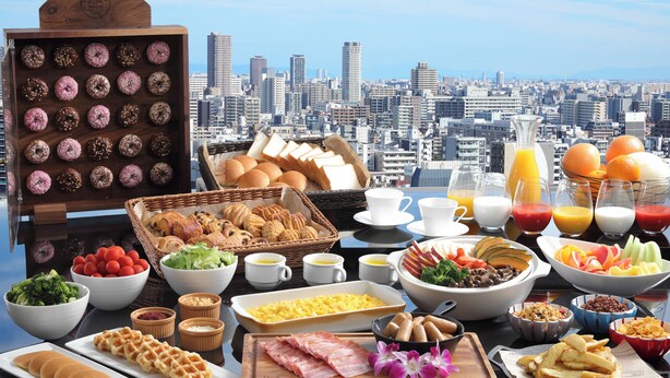 A breakfast buffet with various food items and a cityscape view in the background.