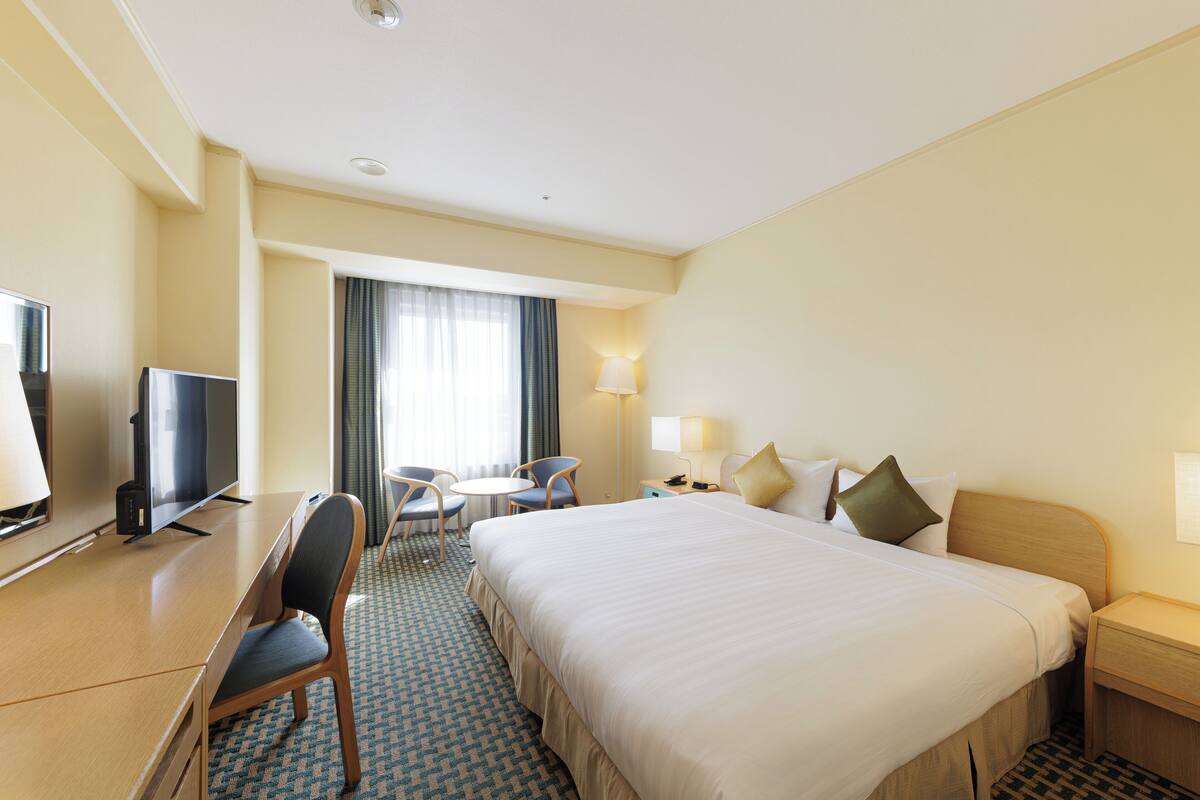 Habitación de hotel con una cama grande, un escritorio con televisor, una silla, una mesita y una lámpara.