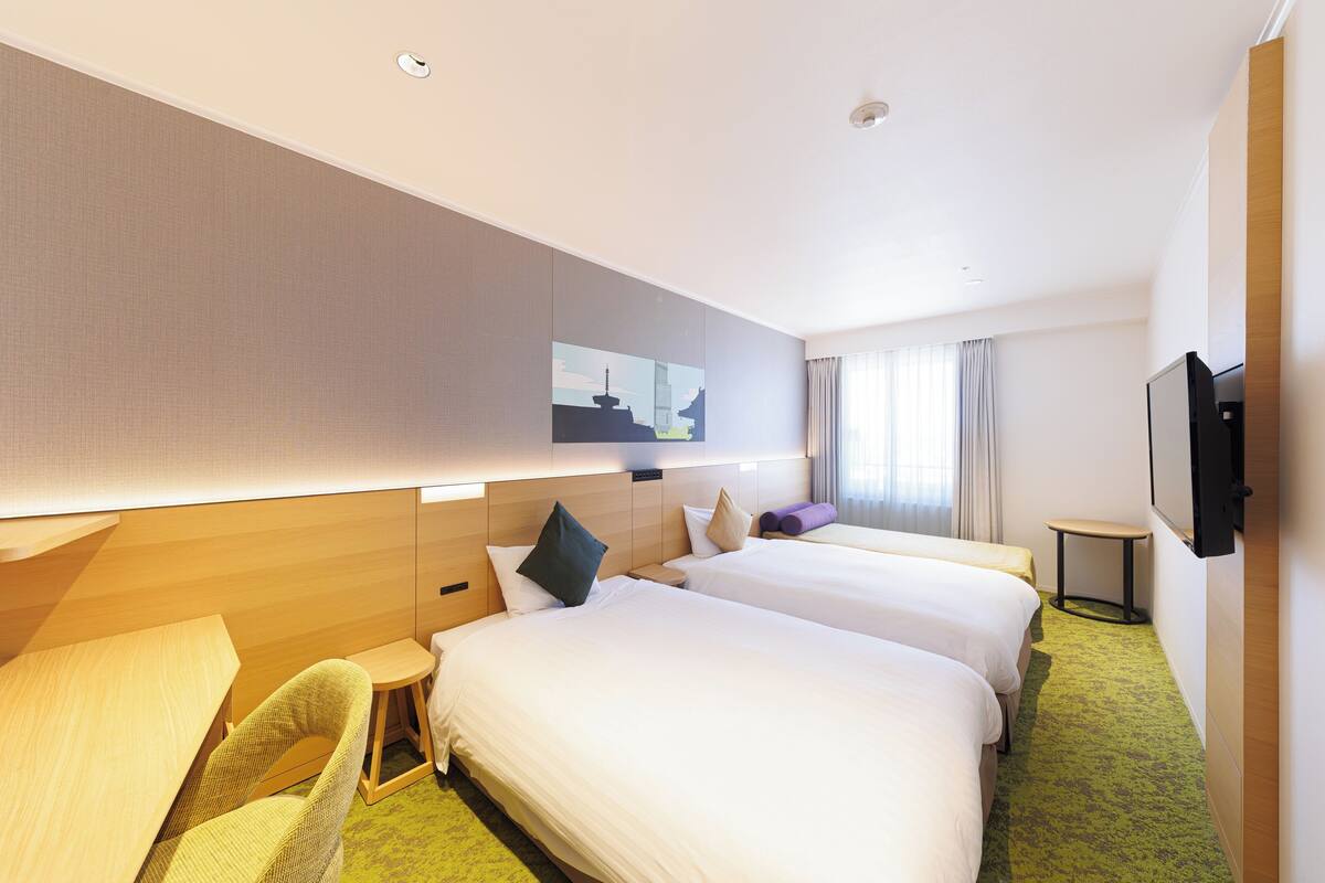 Habitación de hotel con dos camas, una mesita, una silla, televisión y un cuadro en la pared.