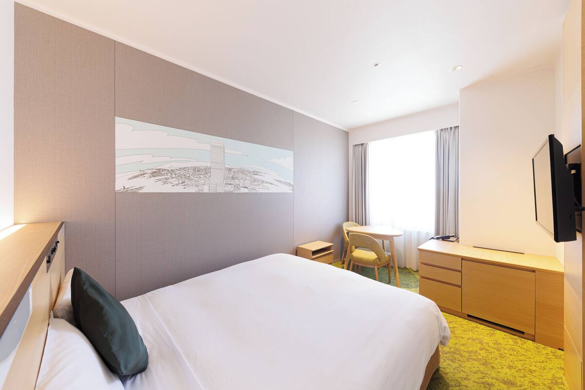 Una habitación de hotel con una cama grande, un escritorio, una silla, un televisor y una ventana con cortinas.