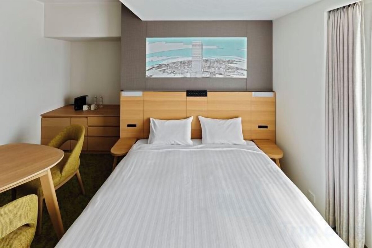 A hotel room with a bed, a desk, a chair, and a painting on the wall.