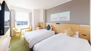 A hotel room with two beds, a desk, a chair, a TV, and a window with a city view.