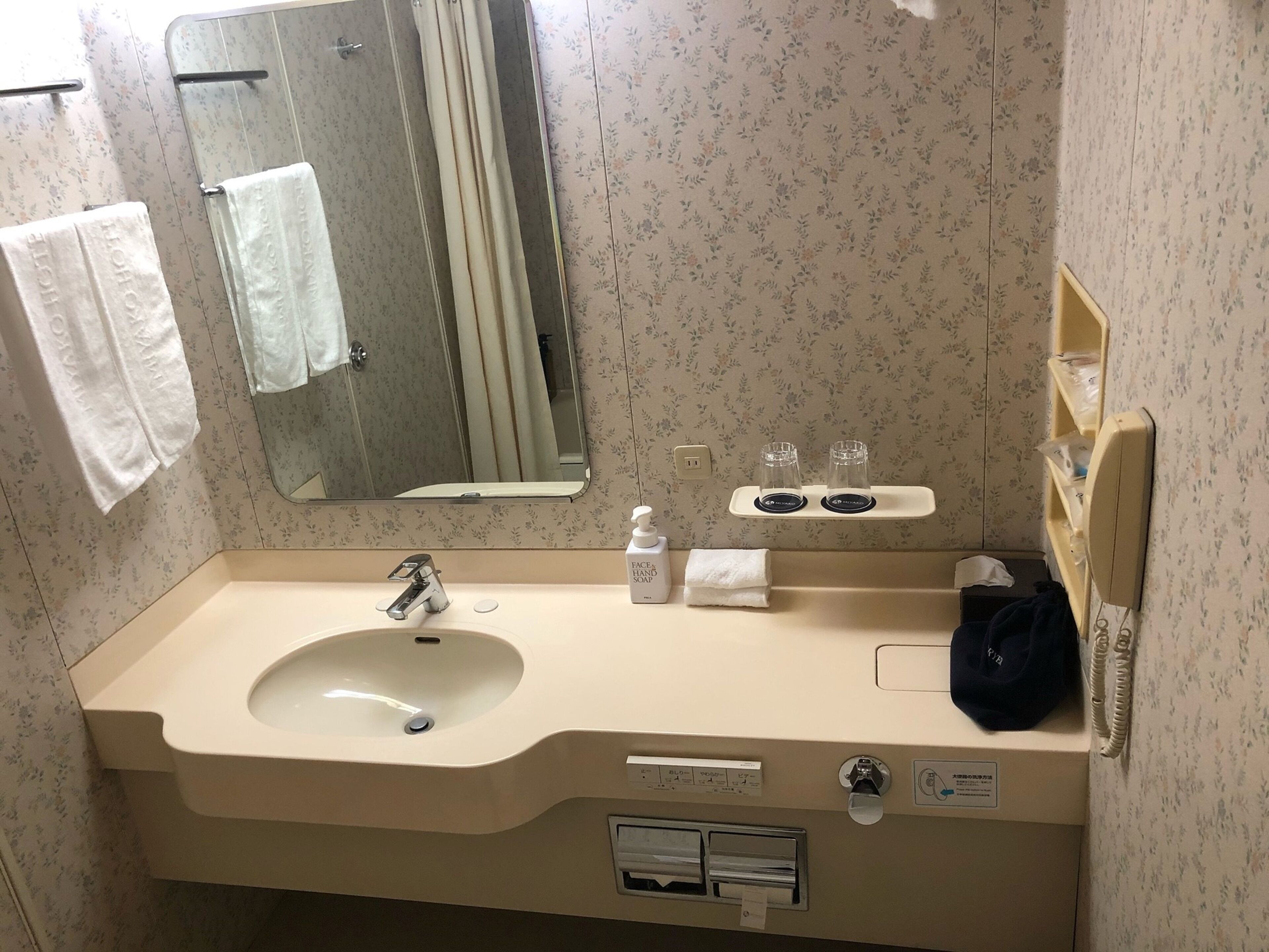 Un bagno con lavandino, specchio, porta asciugamani e dispenser per sapone.
