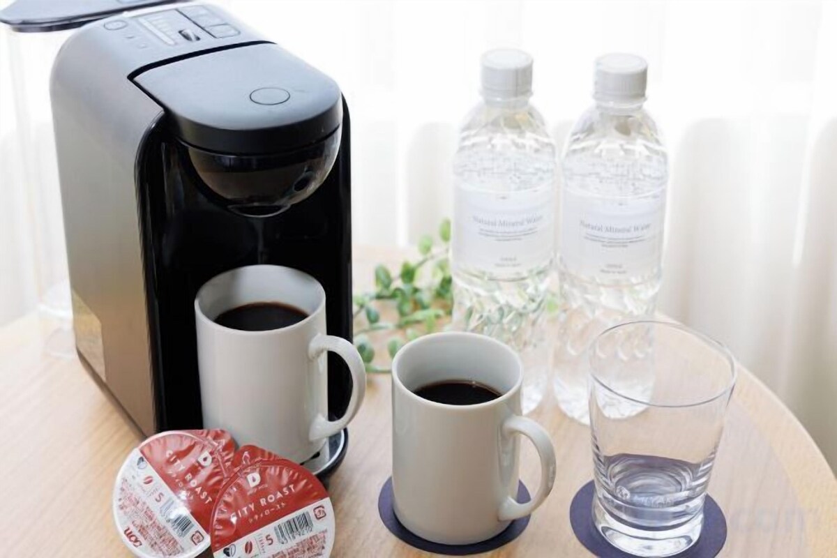 Una cafetera, dos tazas de café, un vaso de agua y dos botellas de agua sobre una mesa de madera.