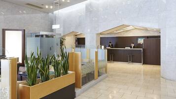 A modern hotel lobby with marble walls, a reception desk, and a seating area with planters.