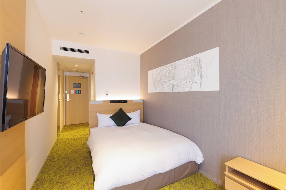 Una habitación de hotel con una cama, un televisor, una mesita de noche y una obra de arte colgada en la pared.