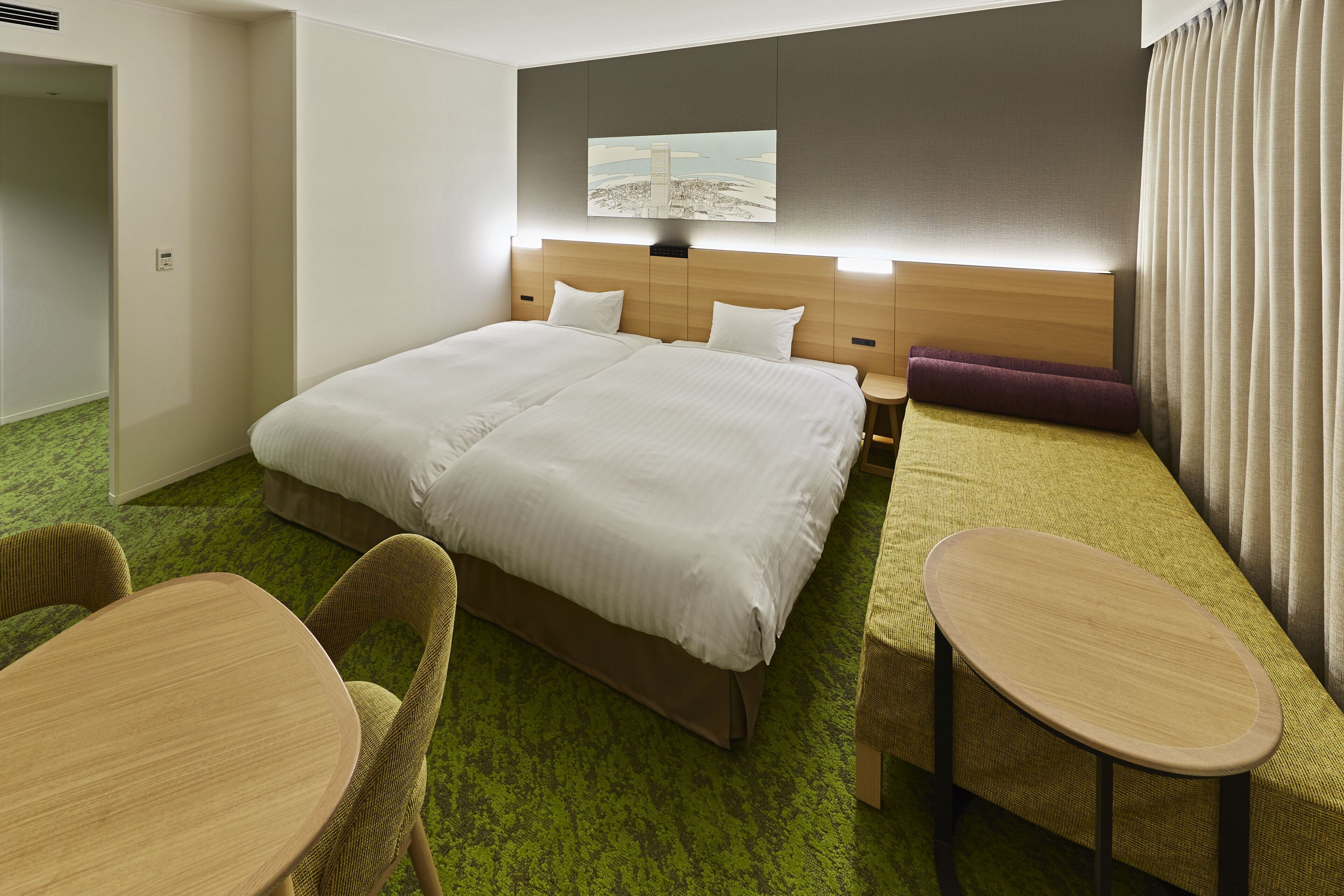 A hotel room with a large bed, a small table, two chairs, a sofa, and a painting on the wall.