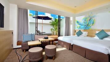 A hotel room with a bed, sofa, two ottomans, a small table, and a large window with a view of greenery.