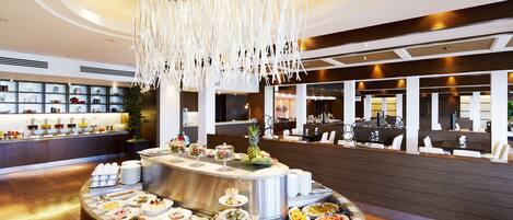 A modern hotel lobby with a central food display, seating area, and a decorative chandelier.
