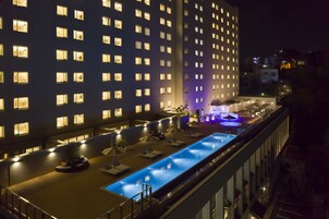Un hotel con piscina, mobiliario exterior y una fachada bien iluminada de noche.