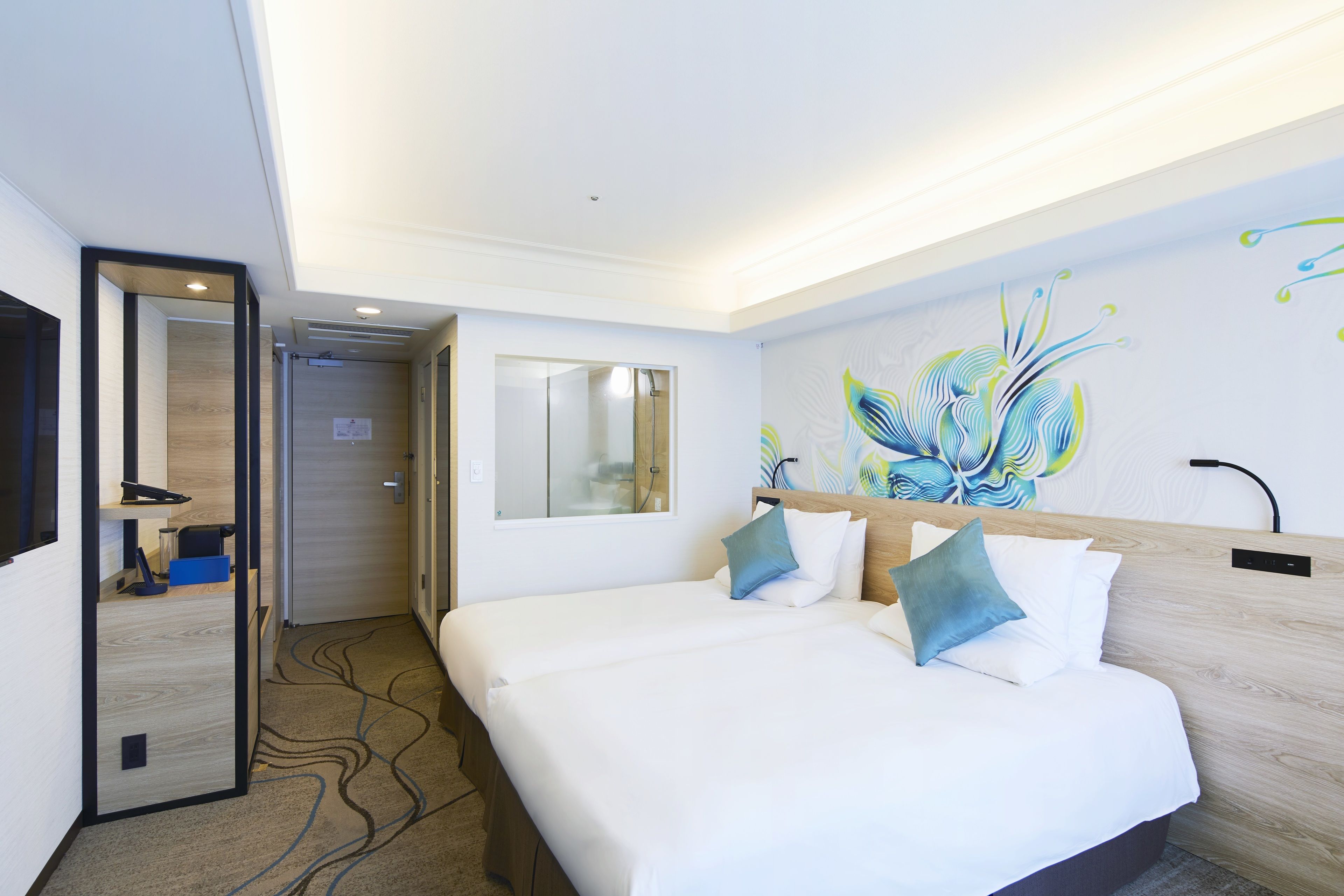A hotel room with a large bed, a mirror, a wall painting, and a door leading to a bathroom.