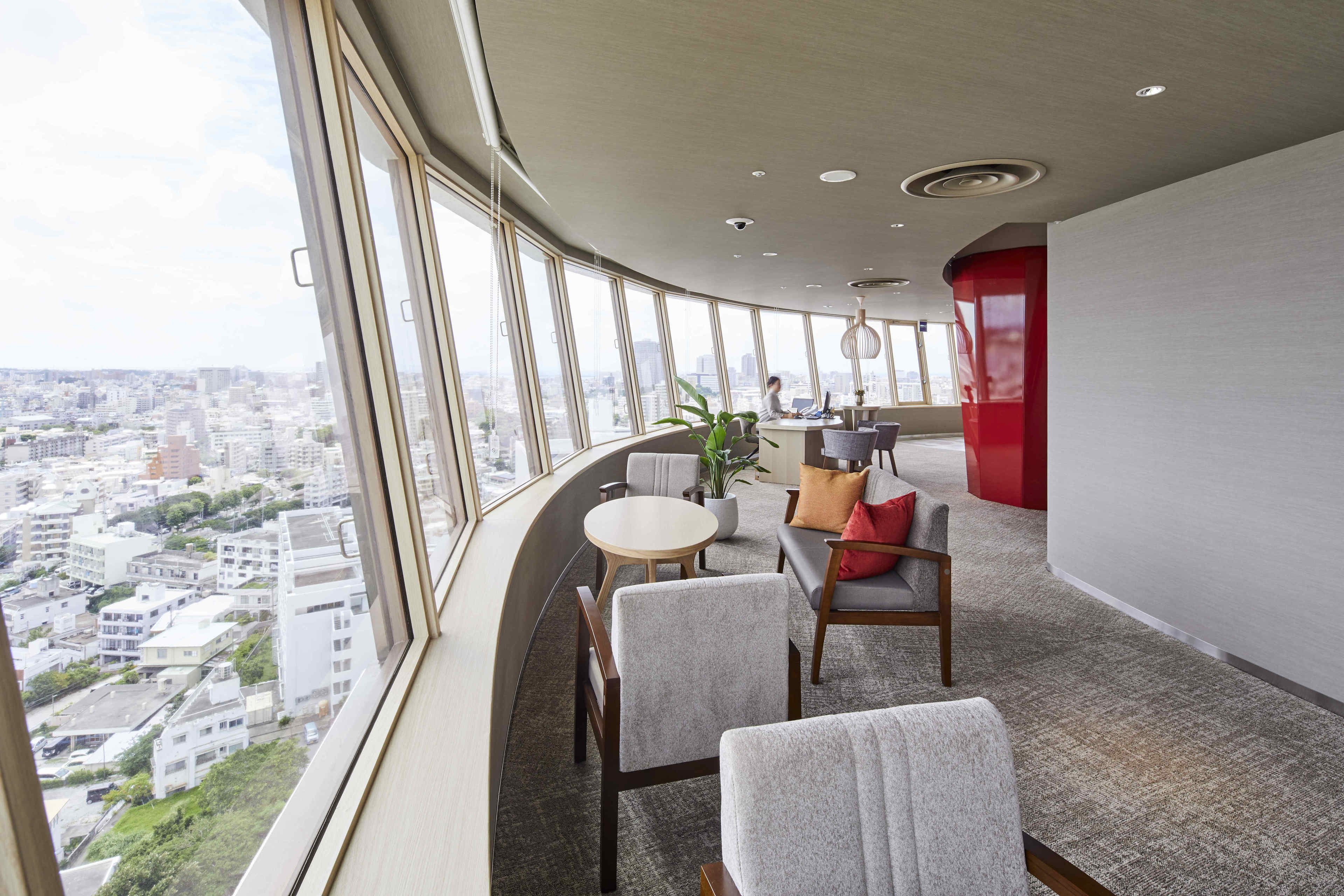 Un salón moderno con techo curvo, ventanas amplias que ofrecen vistas a la ciudad, una mesa redonda y asientos cómodos.