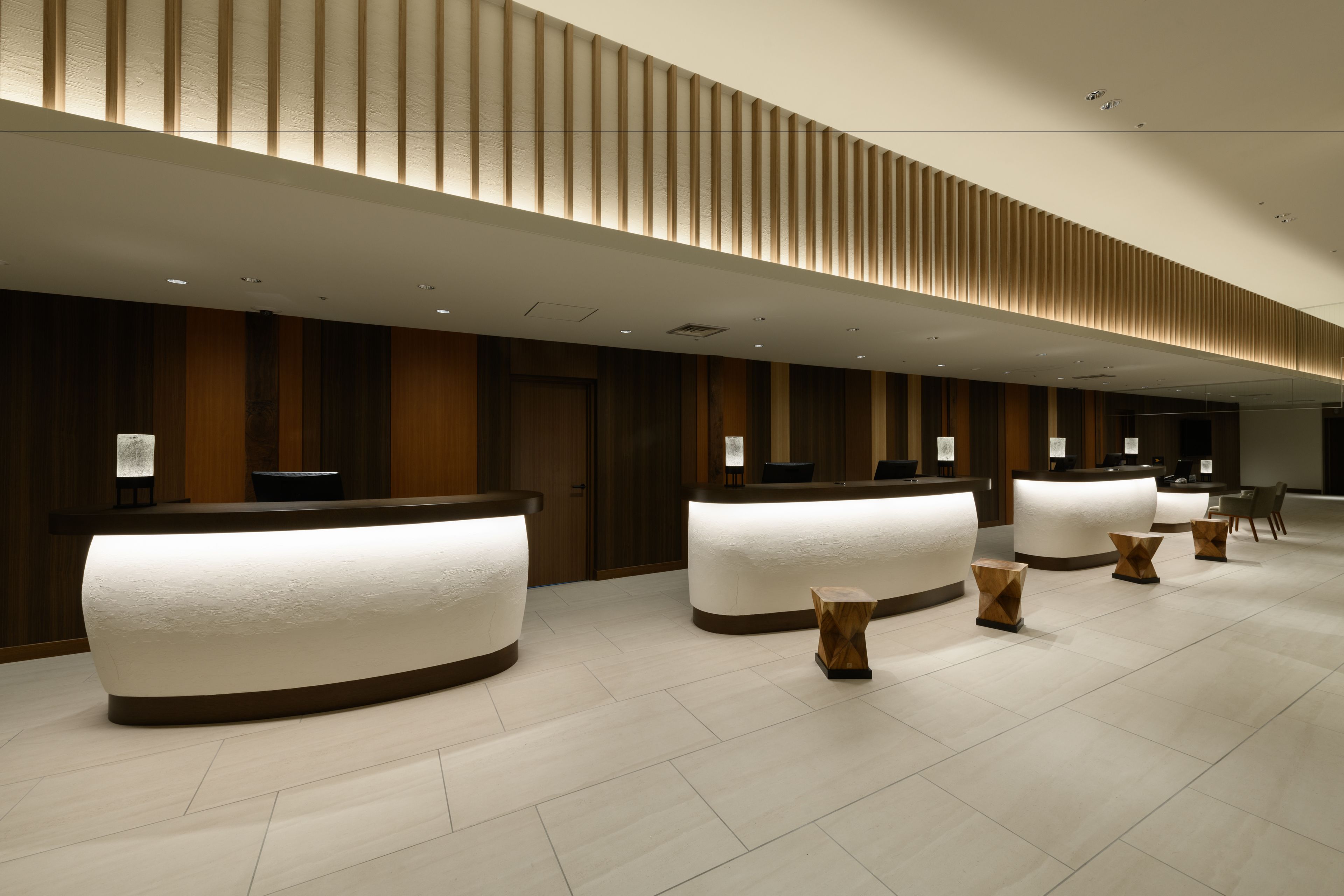 A modern hotel reception area with three curved reception desks, wooden paneling on the walls, and a tiled floor.