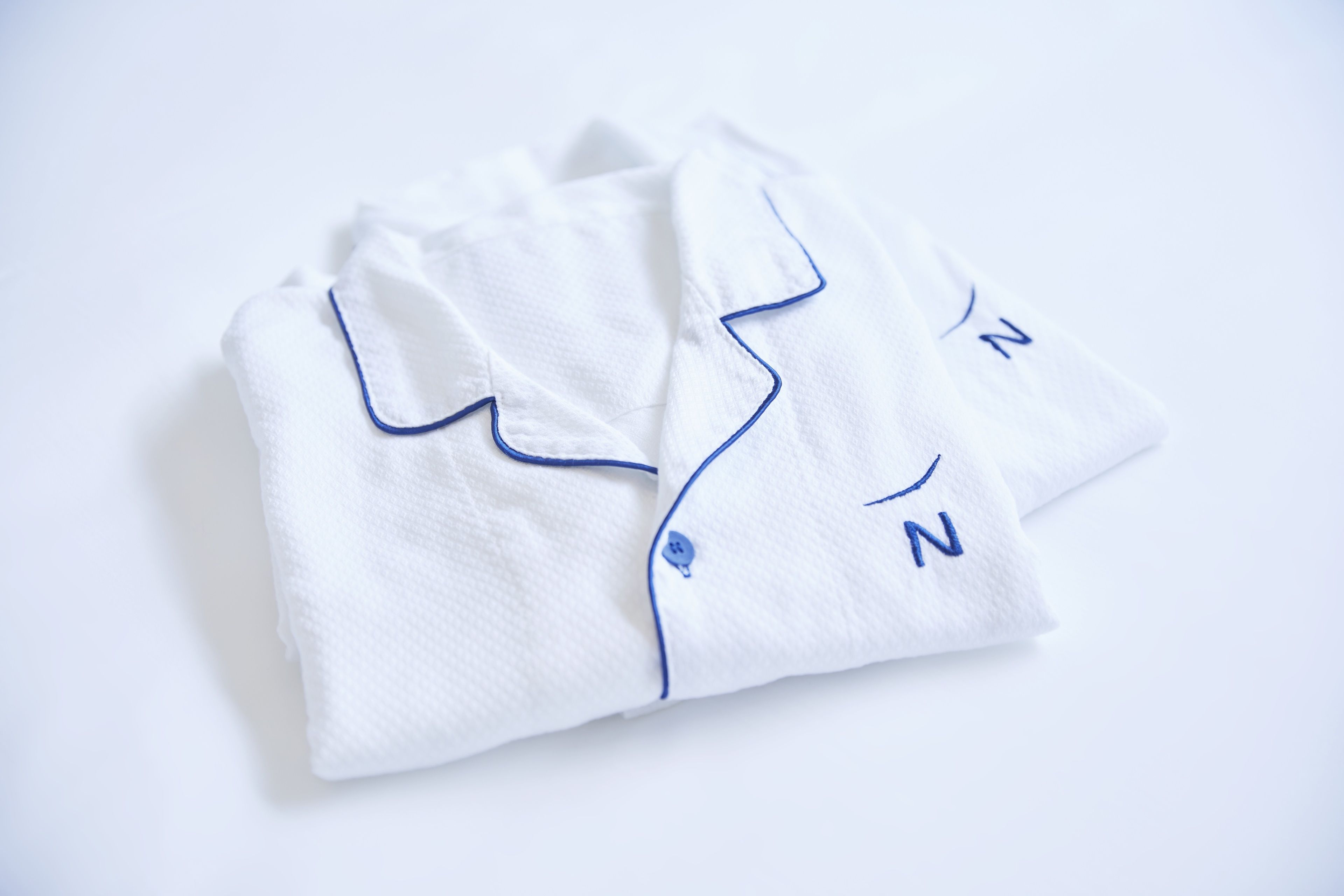 Una camisa blanca bien doblada con ribetes azules y un botón.