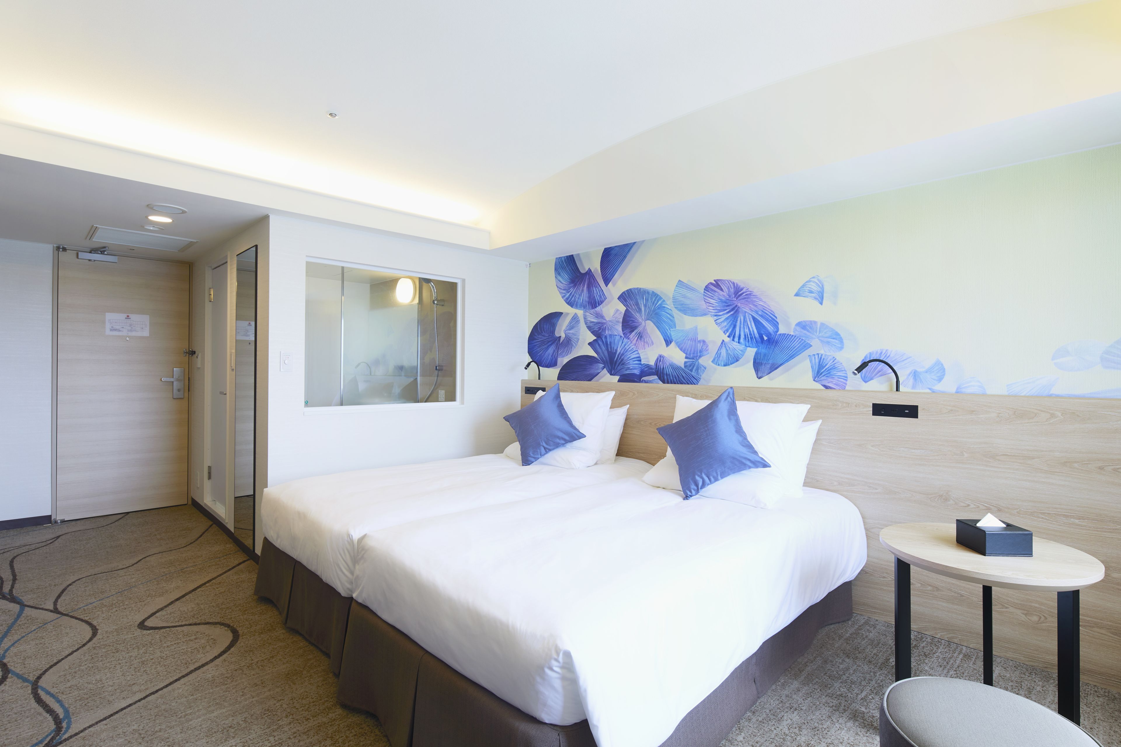 A hotel room with a large bed, a small round table, a mirror, and a wall with a floral mural.