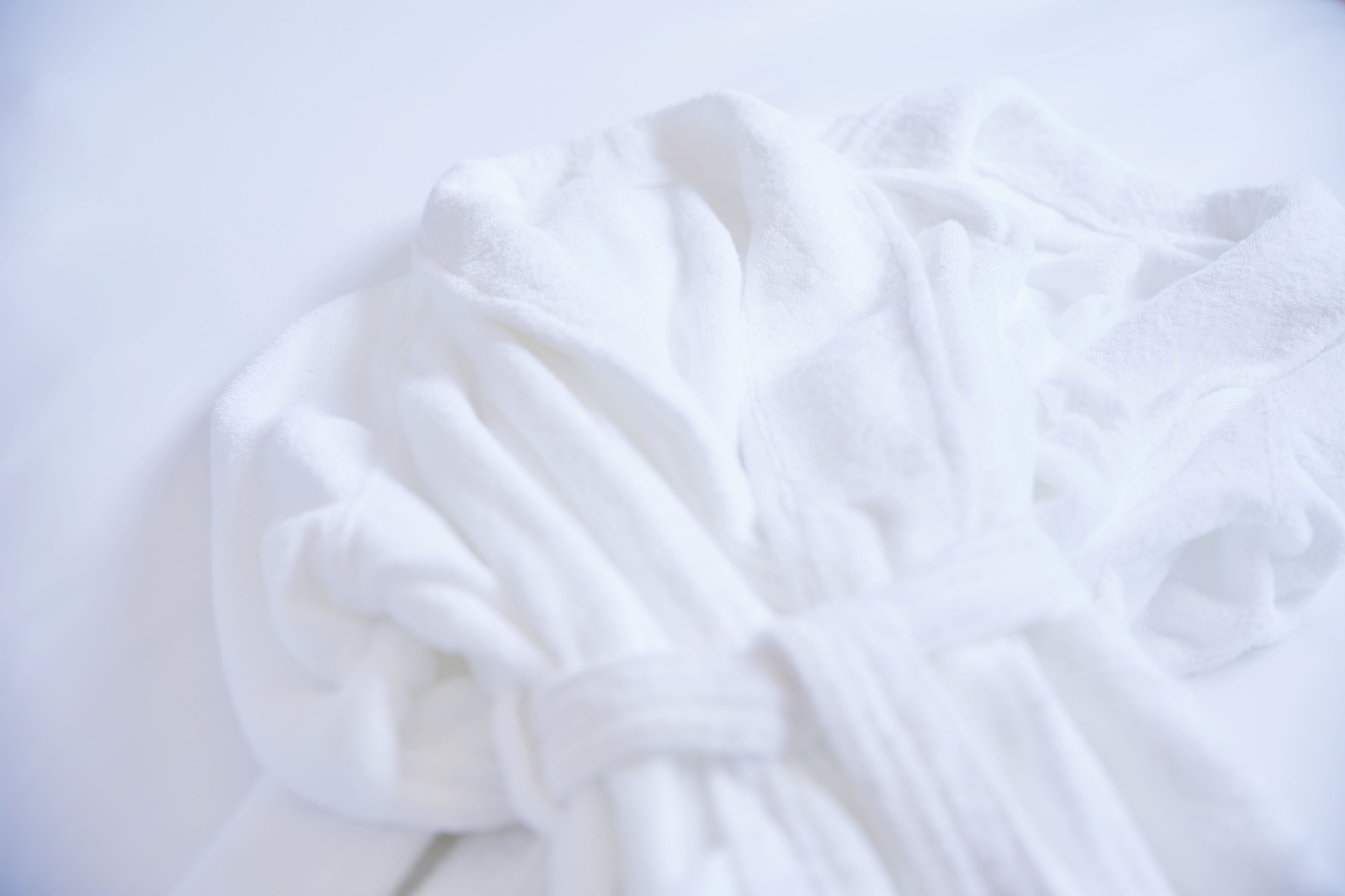 A white bathrobe laid out on a white surface.