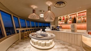 A modern bar area with a central round table, bar stools, and a coffee machine. - INFINISIS NAHA SHURIJO by Hewitt Resort (Naha)