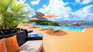 A rooftop pool area with lounge chairs, umbrellas, and a view of the cityscape. - INFINISIS NAHA SHURIJO by Hewitt Resort (Naha)