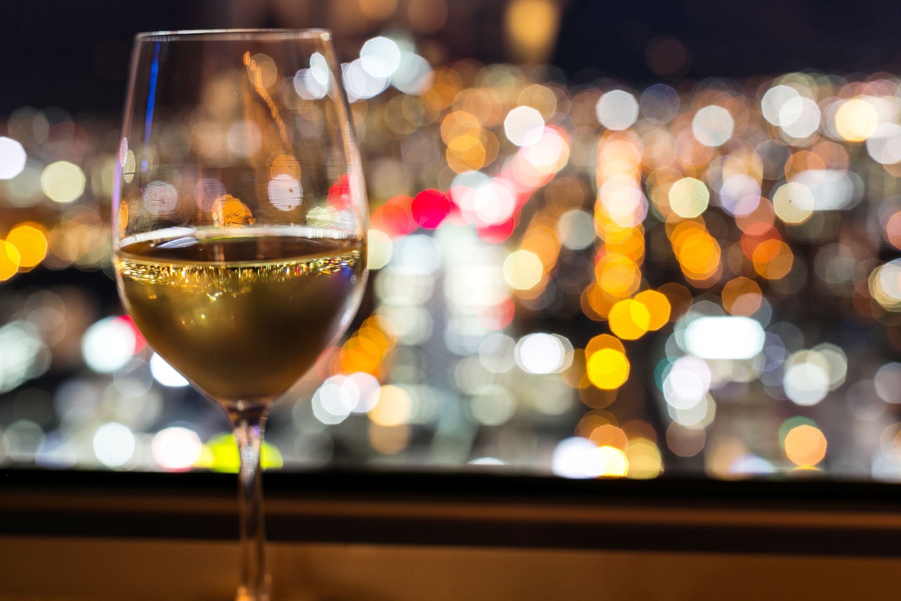 Una copa de vino blanco con un paisaje urbano desenfocado al fondo.