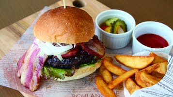 A burger with bacon, lettuce, and a bun, accompanied by fries and two dipping sauces on a wooden board.