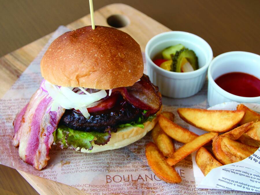A burger with bacon, lettuce, and a bun, accompanied by fries and two dipping sauces on a wooden board.