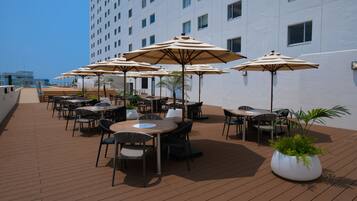 A rooftop terrace with outdoor seating, umbrellas, and potted plants.
