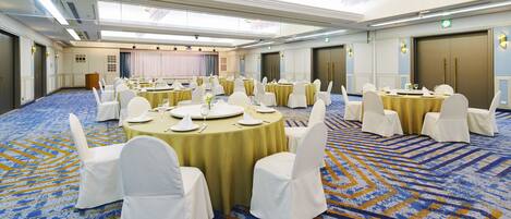 Une grande salle de conférence avec des tables rondes, des chaises blanches et un tapis bleu.