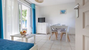 Ein Zimmer mit einem Bett, einem Esstisch mit Stühlen, einem Fernseher auf einem Schrank und einem Fenster mit Vorhängen.