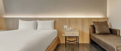 A hotel room with a bed, bedside table, and a sofa.