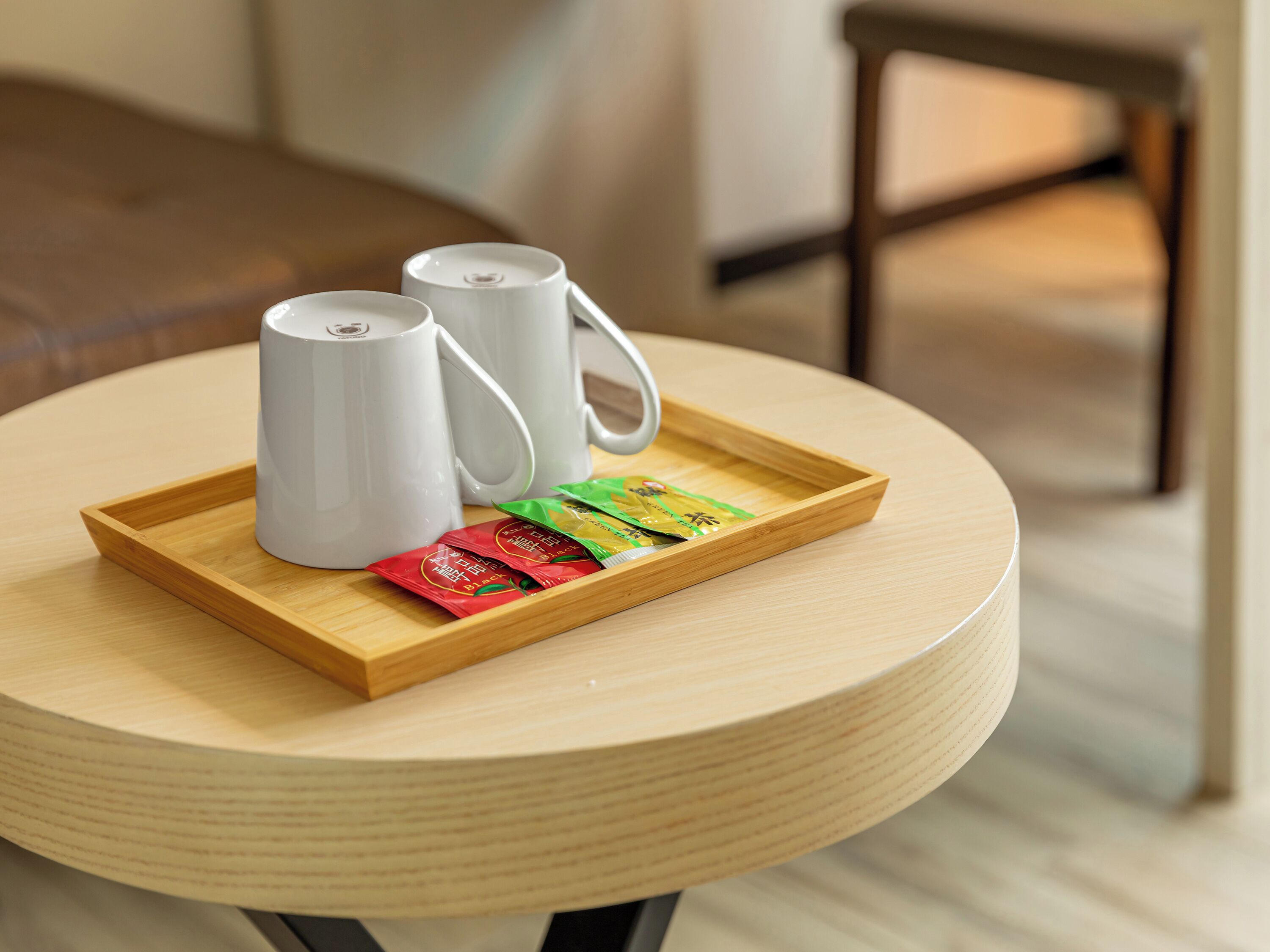Una mesa de madera redonda con dos tazas de cerámica blanca y una bandeja con tres bolsitas de té.