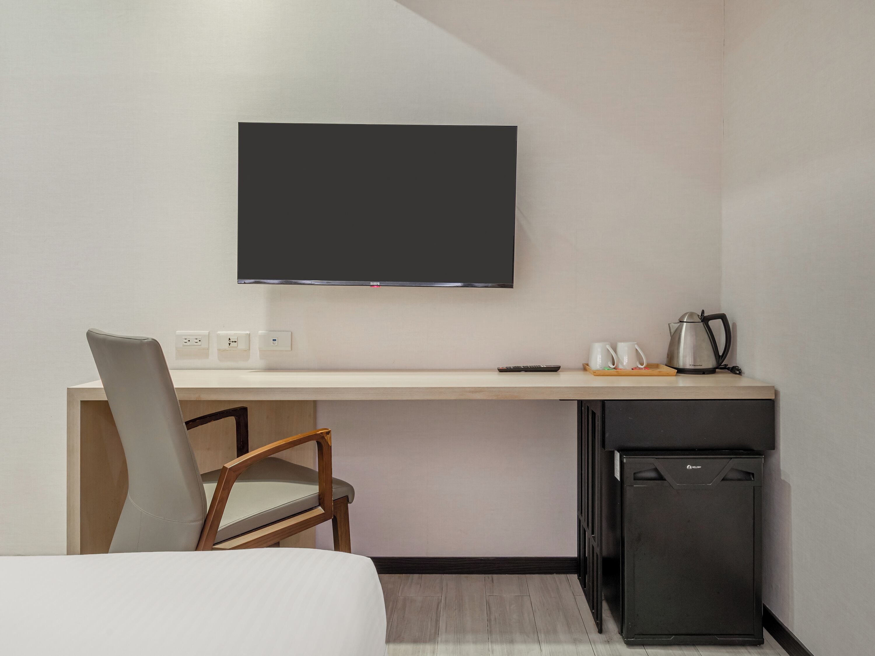A hotel room with a bed, a desk with a television, a refrigerator, and a chair.