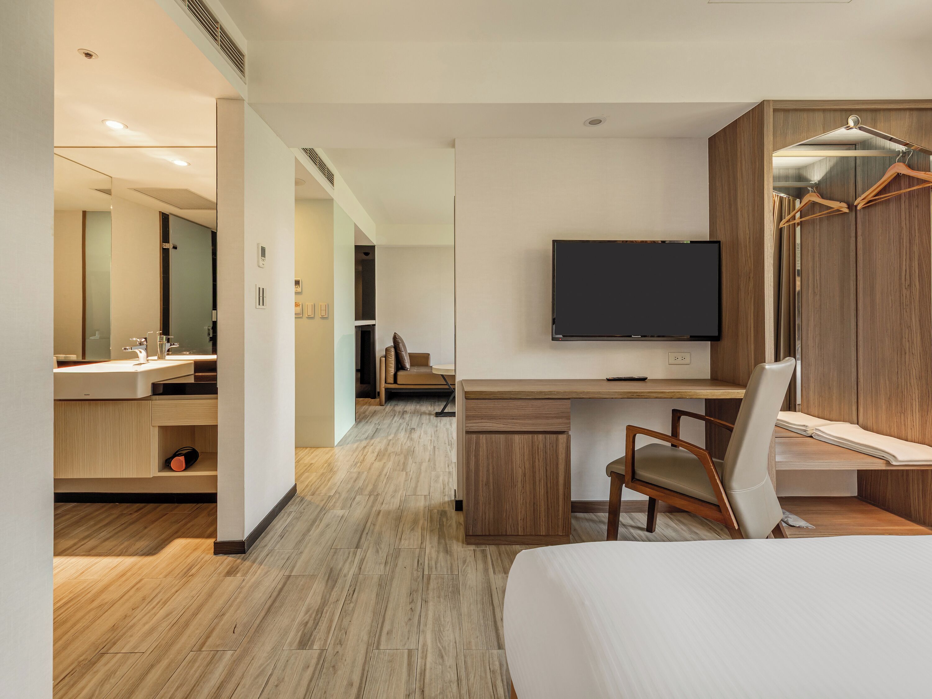 Une chambre d’hôtel moderne équipée d’un lit, d’un bureau, d’une télévision, d’un miroir et d’une armoire.
