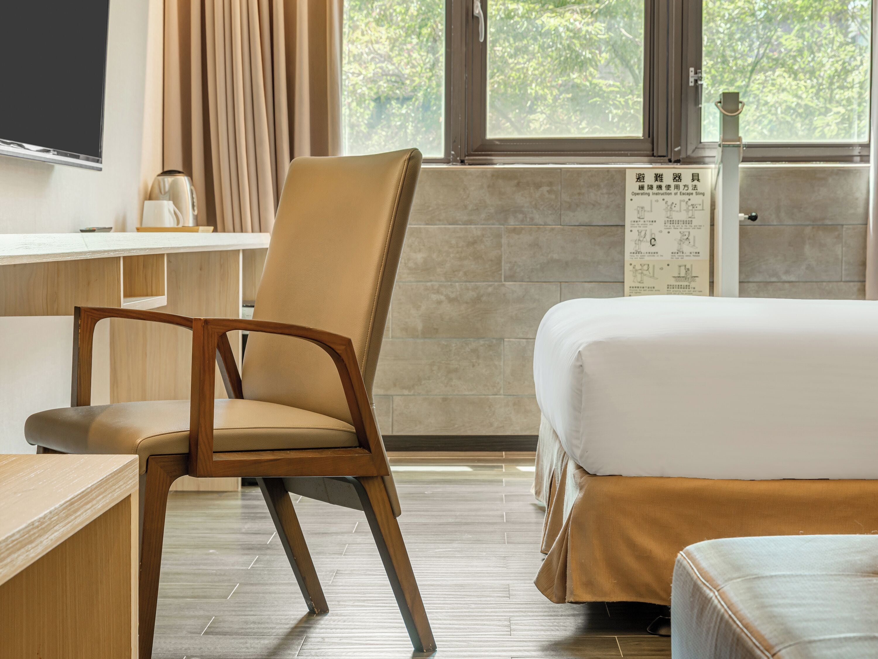 A hotel room with a bed, a chair, a desk, and a window with curtains.