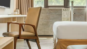 A hotel room with a bed, a chair, a desk, and a window with curtains.