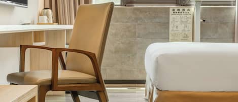 A hotel room with a bed, a chair, a desk, and a window with curtains.