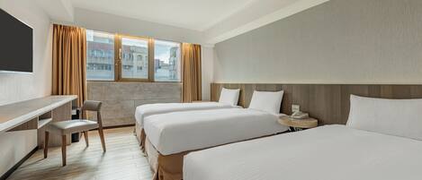 Habitación de hotel con dos camas, un escritorio, una silla, una mesita de noche con lámpara y un amplio ventanal con cortinas.