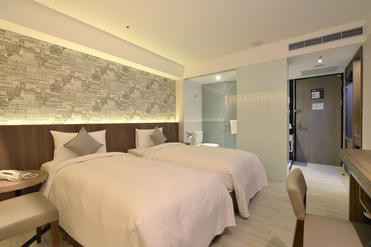 A hotel room with two beds, a desk, a chair, a phone, and a wall with a patterned design.