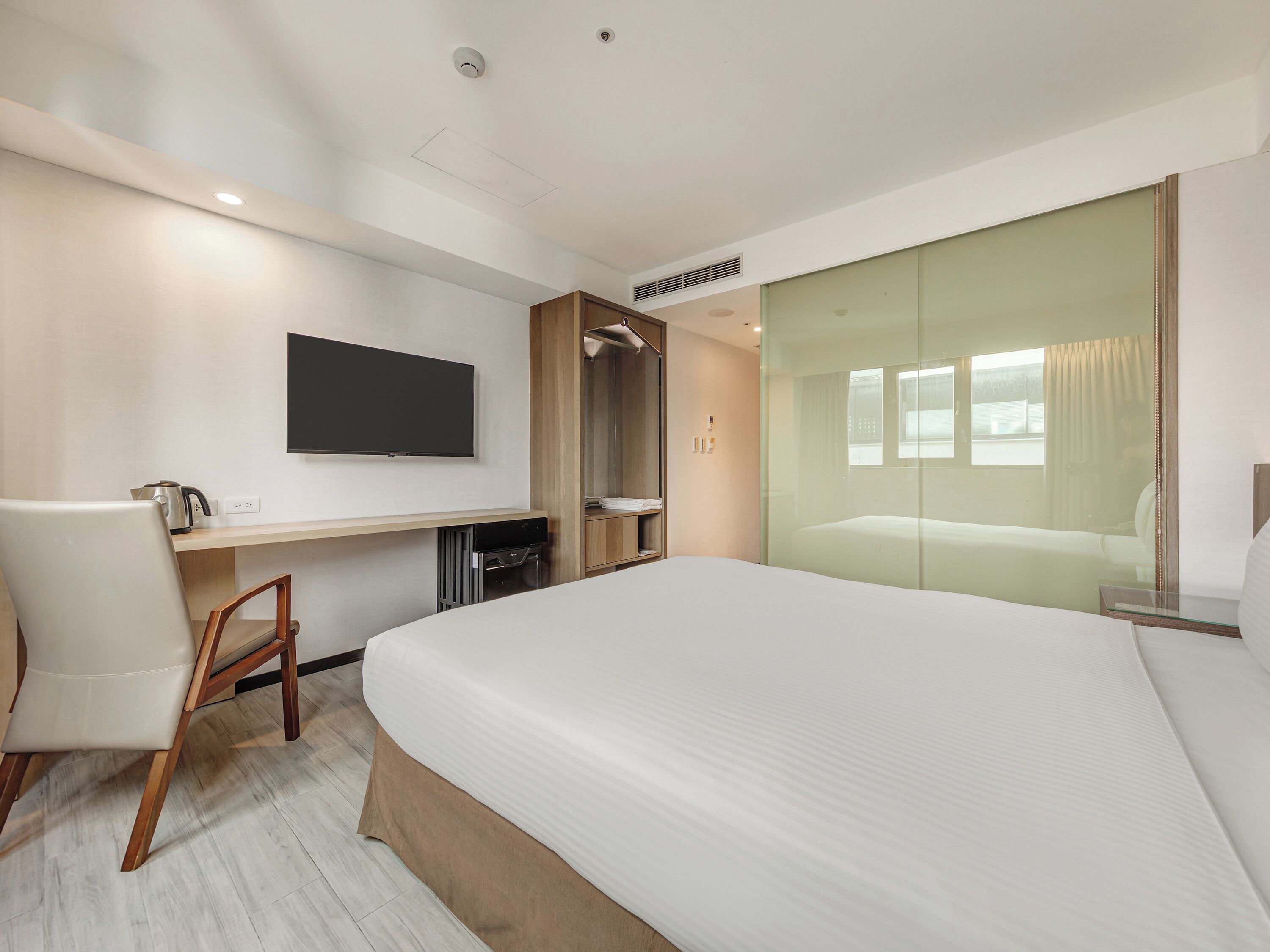 A hotel room with a bed, a desk, a television, and a sliding glass door.