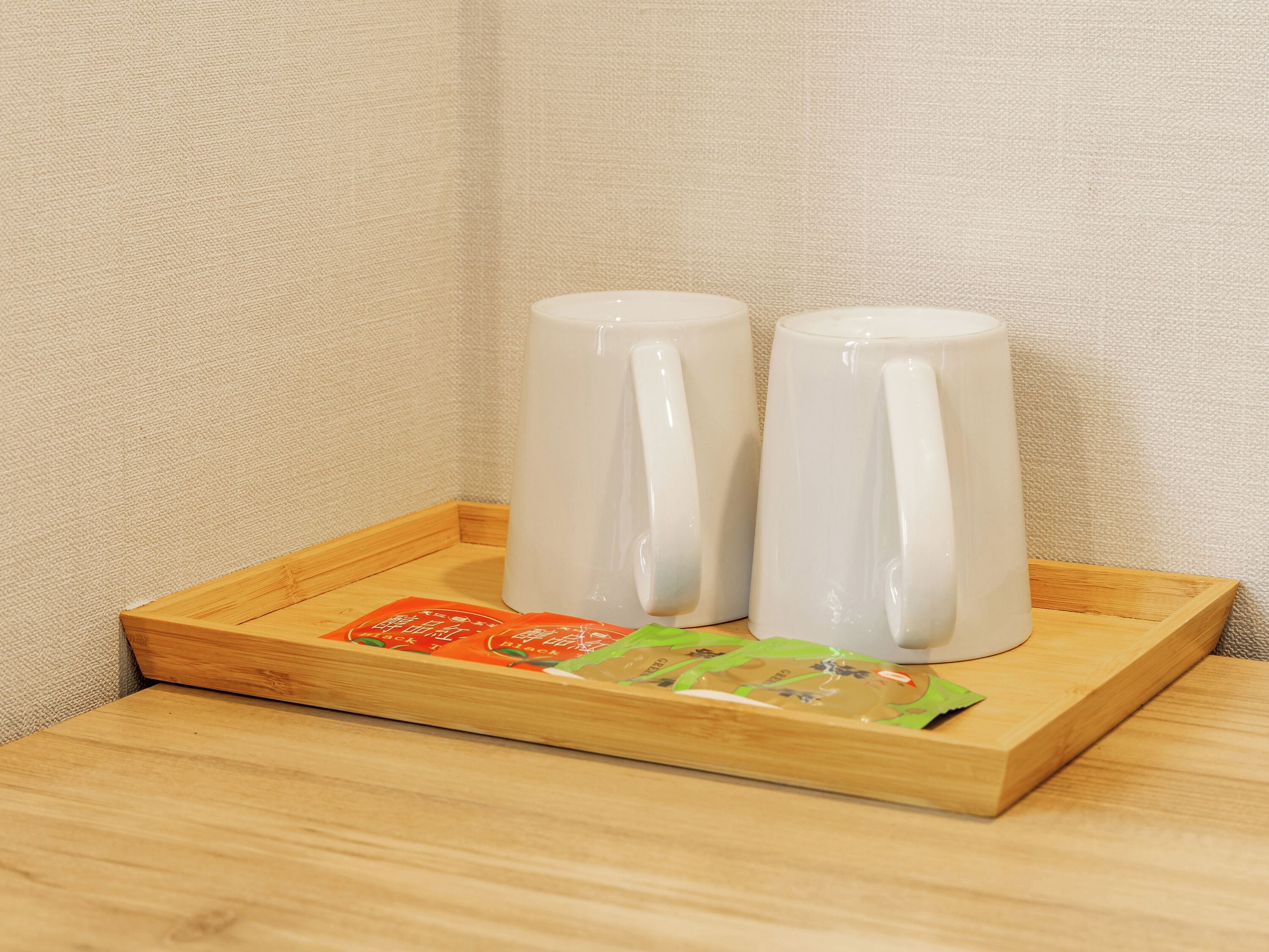 A wooden tray with two white ceramic mugs and a packet of snacks.