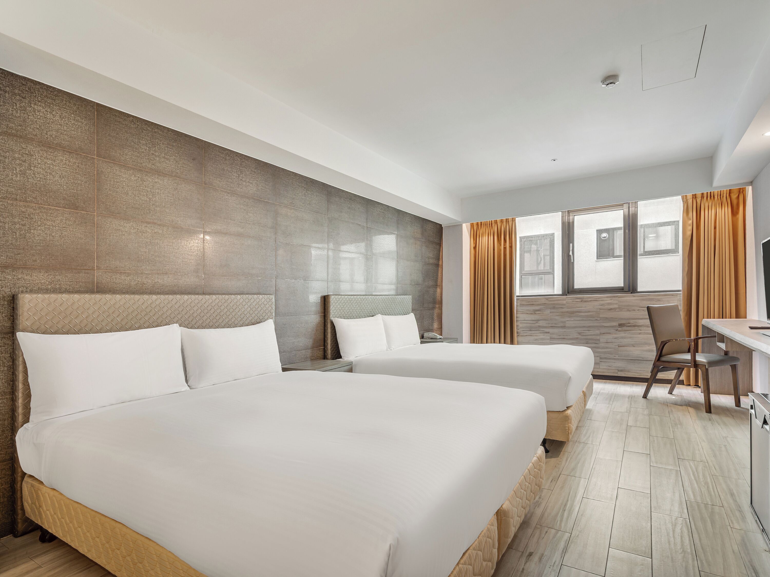 A hotel room with two beds, a desk, and a chair.