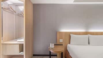 A hotel room with a bed, a bedside table with a phone, a wooden wardrobe, and a mirror.