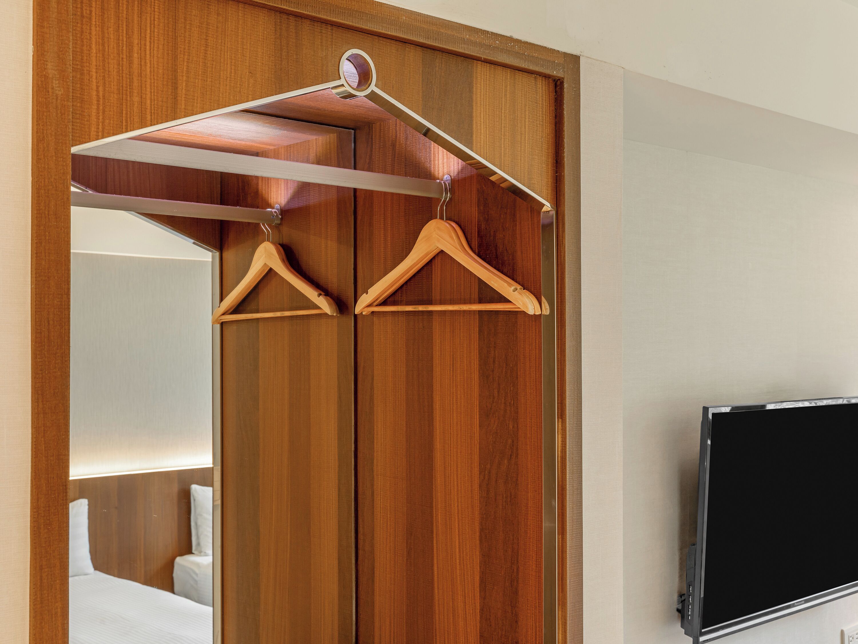 A hotel room with a wooden wardrobe, a mirror, and a television.