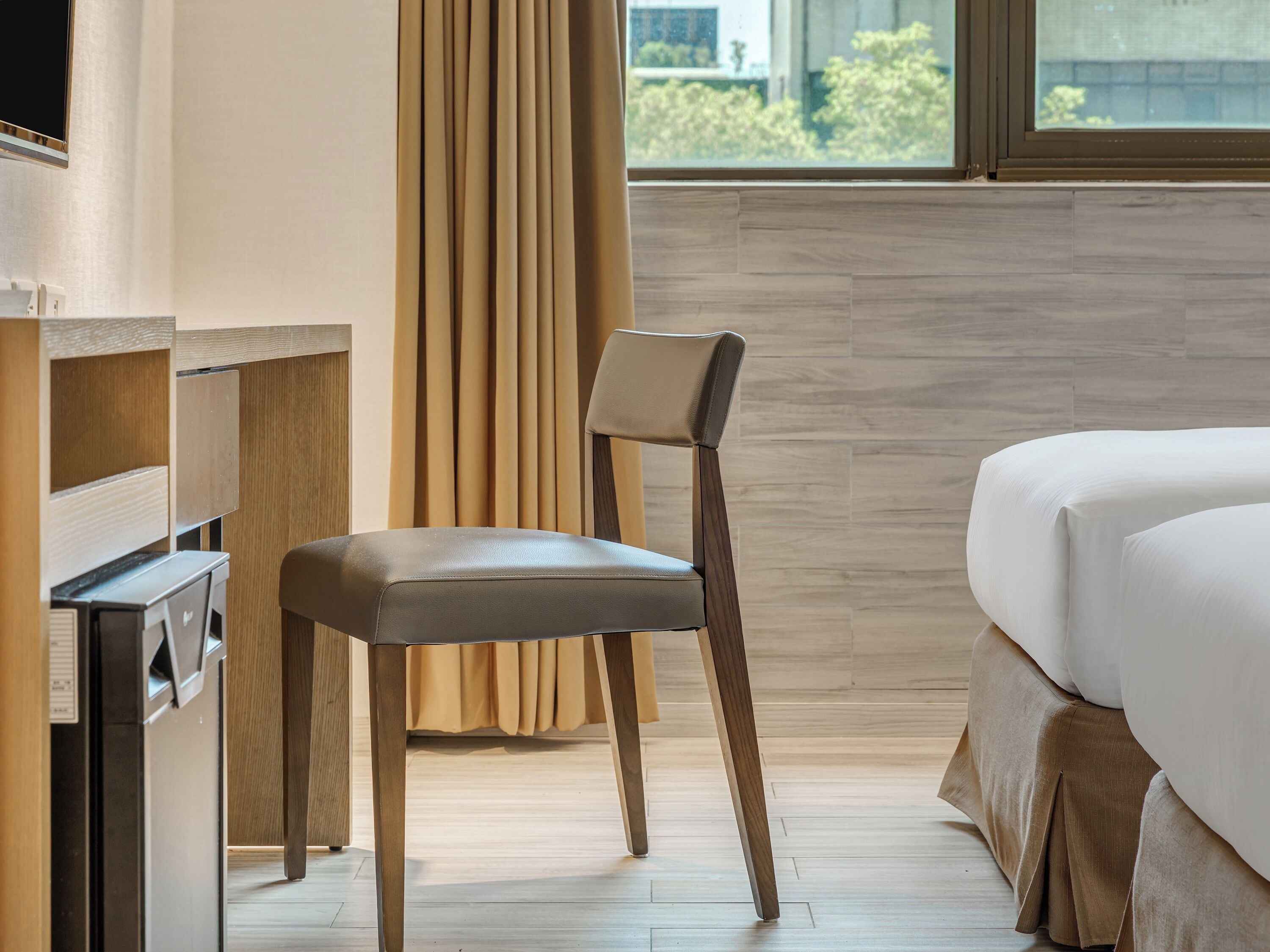 A hotel room with a bed, a chair, a desk, and a window with curtains.