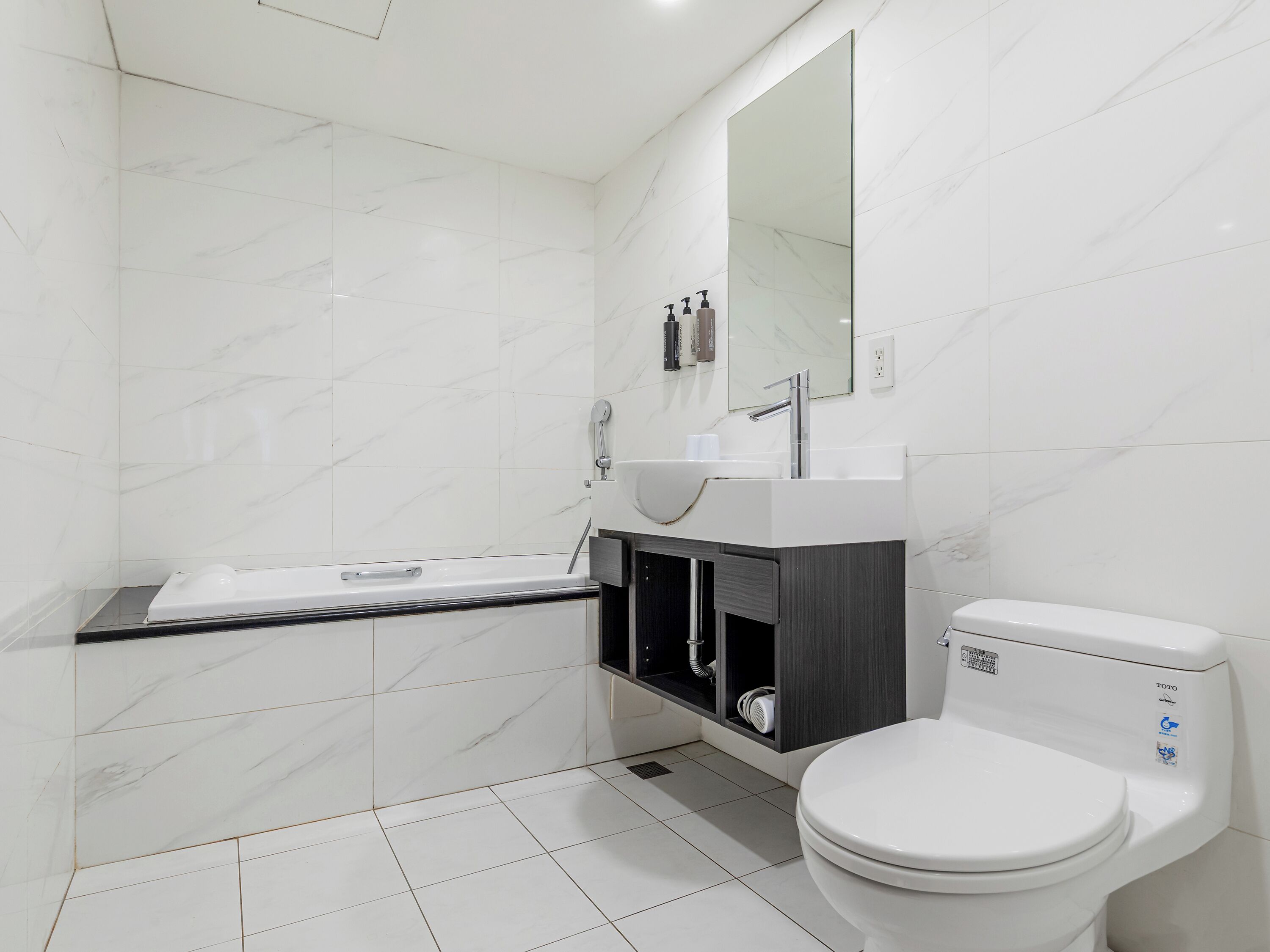 A modern bathroom with a white toilet, a sink with a mirror above it, and a bathtub.