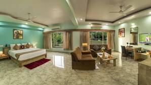 Habitación de hotel con cama, sofá, escritorio, televisión y ventanas amplias con cortinas.