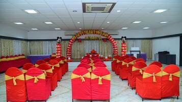 A conference room with rows of red chairs with yellow sashes, a stage with a 'Happy Birthday Amanya' banner, and a backdrop with balloons.