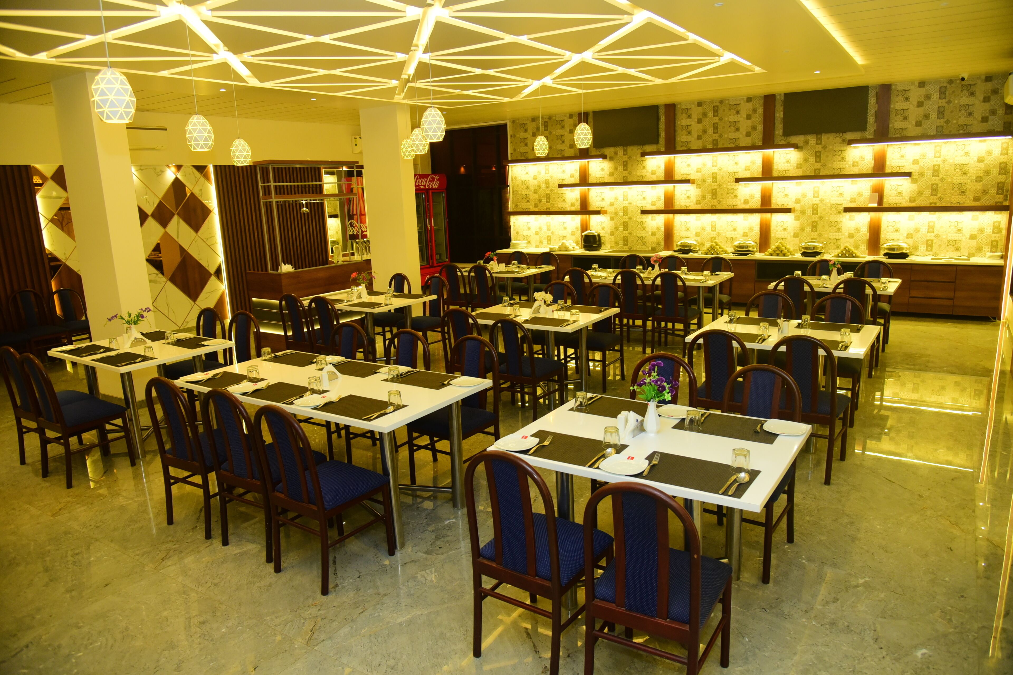 A restaurant with multiple tables and chairs, geometric ceiling lights, and a patterned wall.