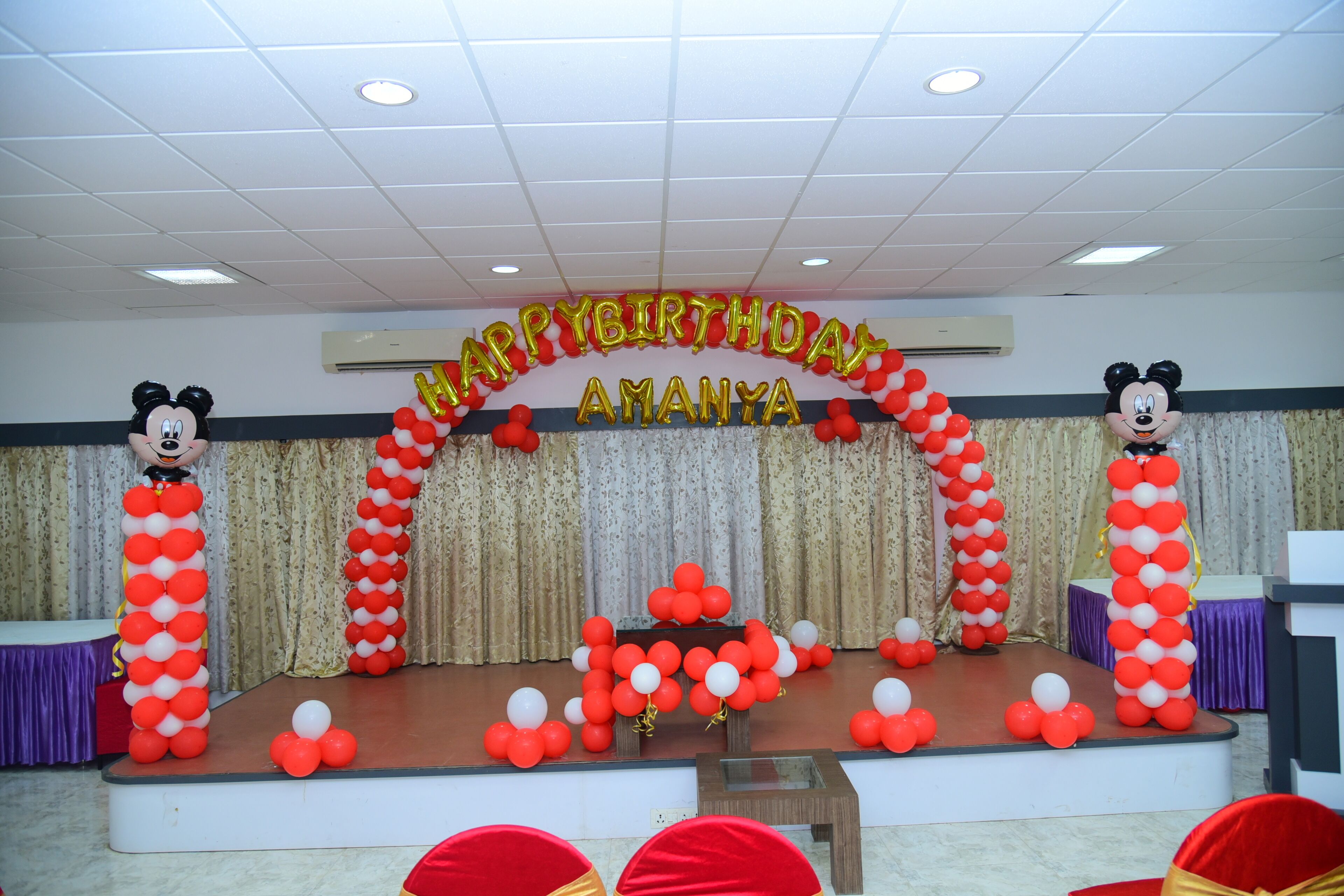 A stage with a 'Happy Birthday Amanya' banner, balloons, and two Mickey Mouse figures.